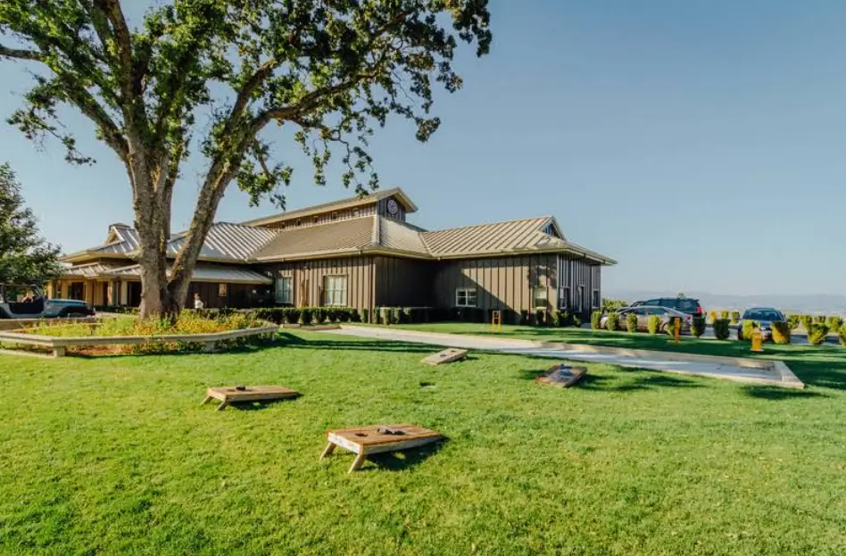 Outdoor lawn at Boatique Winery with cornhole games, green grass, and the winery building under a clear sky