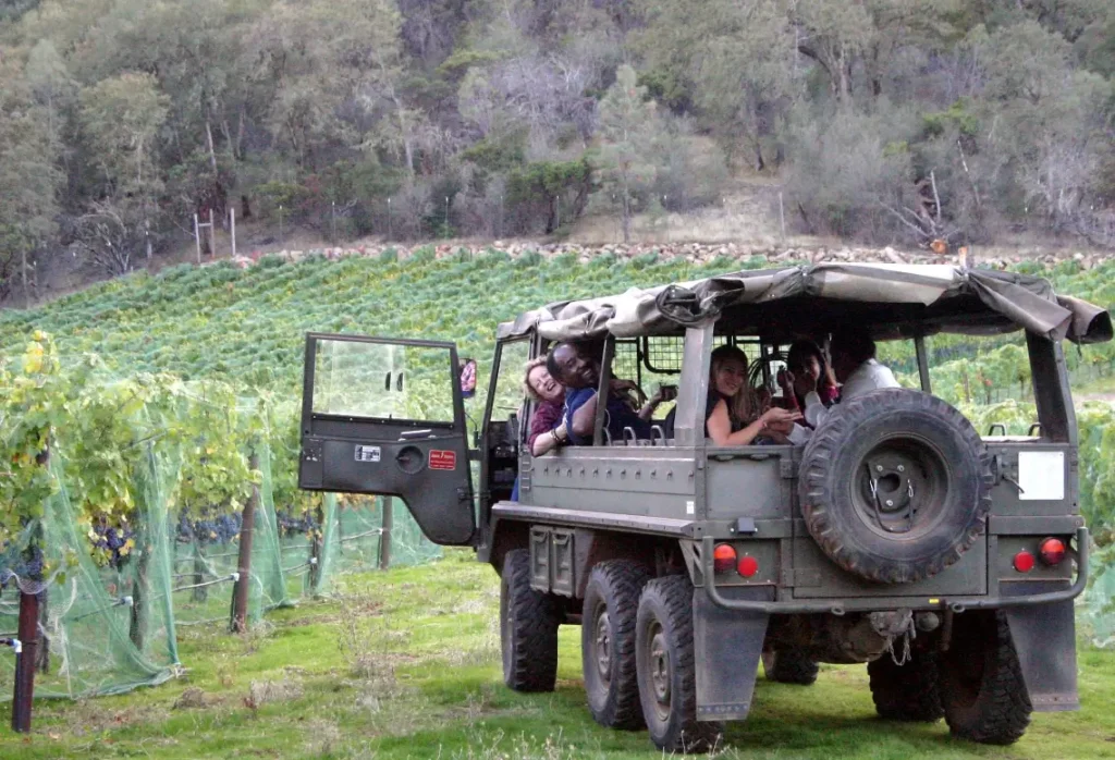 Group of people in an open-air military-style vehicle touring a vineyard