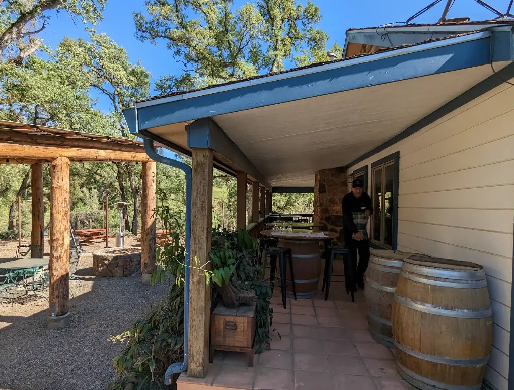 Man standing near wine barrels on a shaded winery porch