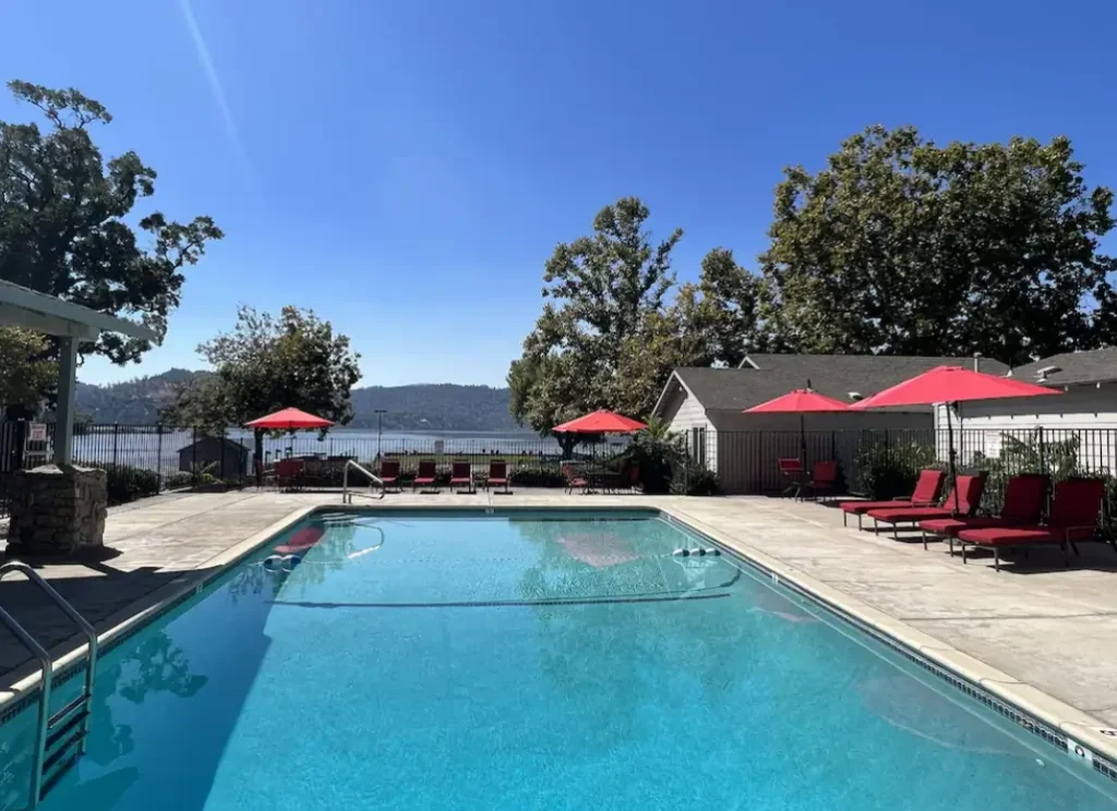 Outdoor pool with red umbrellas near lake and hills
