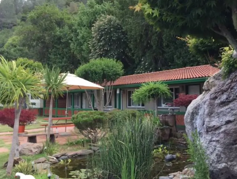Garden view of a small motel surrounded by greenery and a pond