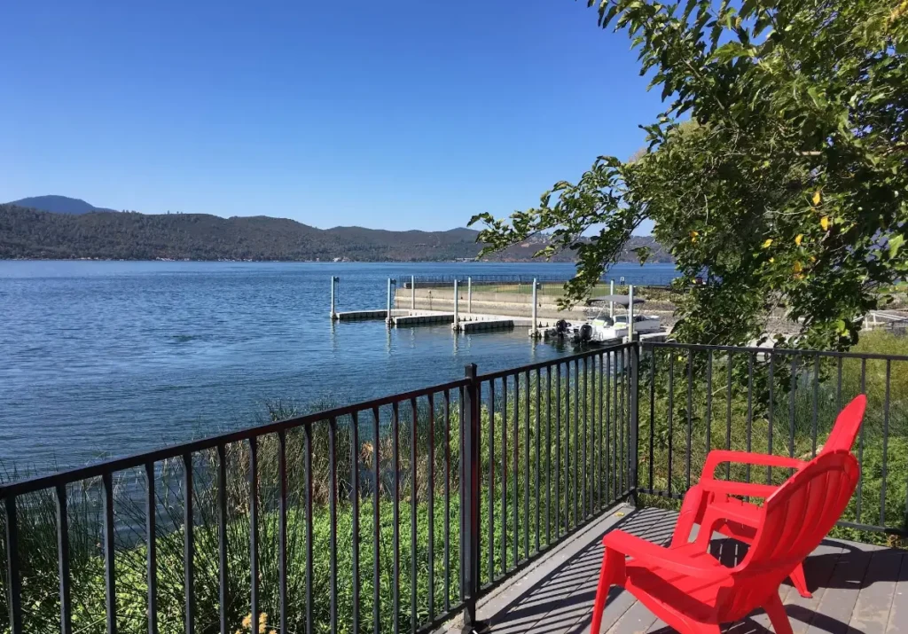 Two red chairs on a deck facing lake and boat dock
