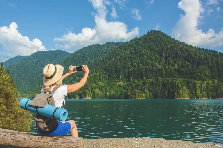 Woman taking photo of forested mountain across a lake